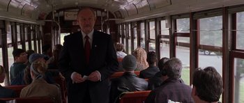 Movie still from “Runaway Jury” (2003), directed by Gary Fleder – A man in a suit and red tie standing on a train; Medium shot, Over the shoulder angle