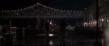 Movie still from “Runaway Jury” (2003), directed by Gary Fleder – Two people standing on a sidewalk near a bridge at night; Extreme Wide shot, Low angle