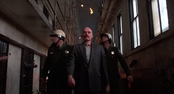 Movie still from “Runaway Train” (1985), directed by Andrey Konchalovskiy – A man in a suit standing between two police officers; Wide shot, Low angle