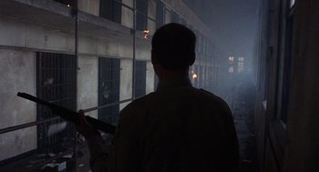 Movie still from “Runaway Train” (1985), directed by Andrey Konchalovskiy – A man standing in front of a building holding a cell phone; Wide shot, Low angle