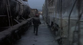 Movie still from “Runaway Train” (1985), directed by Andrey Konchalovskiy – A man walking down a snowy street next to a train; Wide shot, High angle