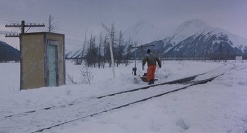 Movie still from “Runaway Train” (1985), directed by Andrey Konchalovskiy – A man riding a snowboard down the side of a snow covered slope; Extreme Wide shot, Low angle