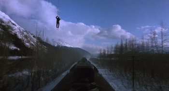 Movie still from “Runaway Train” (1985), directed by Andrey Konchalovskiy – A person is hanging from a crane above a train track; Wide shot, Low angle