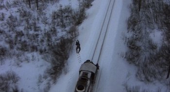 Movie still from “Runaway Train” (1985), directed by Andrey Konchalovskiy – A person is climbing up a ladder on the side of a snow covered train; Extreme Wide shot, Overhead angle