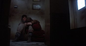 Movie still from “Runaway Train” (1985), directed by Andrey Konchalovskiy – A man sitting on a chair holding a stuffed animal; Wide shot, Overhead angle