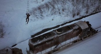 Movie still from “Runaway Train” (1985), directed by Andrey Konchalovskiy – A man is hanging from a ladder while riding a train; Wide shot, Overhead angle