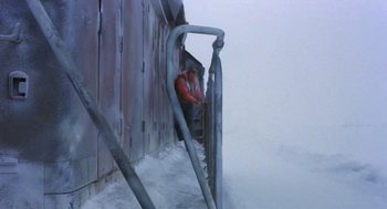 Movie still from “Runaway Train” (1985), directed by Andrey Konchalovskiy – A man sitting on top of a railing next to a building; Wide shot, Low angle