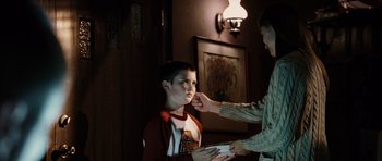 Movie still from “Running Scared” (2006), directed by Wayne Kramer – A man putting makeup on a young boy's face; Medium shot, Over the shoulder angle