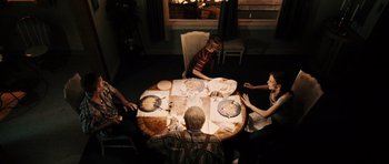 Movie still from “Running Scared” (2006), directed by Wayne Kramer – A group of people sitting around a table with food; Wide shot, High angle