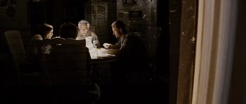 Movie still from “Running Scared” (2006), directed by Wayne Kramer – Two men sitting at a table in a dark room looking at their phones; Medium shot, Over the shoulder angle