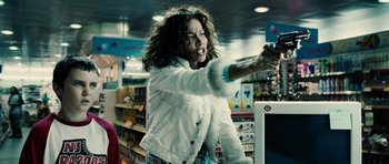 Movie still from “Running Scared” (2006), directed by Wayne Kramer – A woman in a white jacket is playing a video game in a store; Medium shot, Over the shoulder angle
