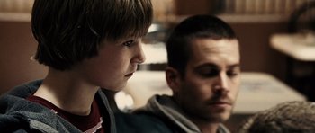 Movie still from “Running Scared” (2006), directed by Wayne Kramer – A young boy and a young man sitting next to each other; Close Up shot, Over the shoulder angle