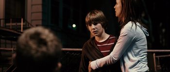 Movie still from “Running Scared” (2006), directed by Wayne Kramer – A boy and a woman standing next to each other in front of a fence; Medium shot, Over the shoulder angle