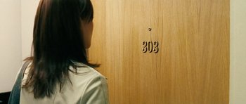 Movie still from “Running Scared” (2006), directed by Wayne Kramer – A woman standing in front of a wooden wall with the number " 3 0 3 " painted on it; Extreme Close Up shot, High angle