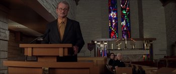 Movie still from “Rushmore” (1998), directed by Wes Anderson – A man standing at the top of a podium in front of stained glass windows; Medium shot, Low angle