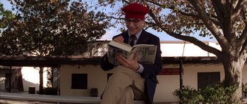 Movie still from “Rushmore” (1998), directed by Wes Anderson – A man sitting on a bench while reading a book; Medium shot, High angle