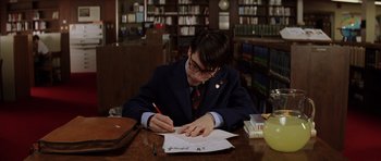 Movie still from “Rushmore” (1998), directed by Wes Anderson – A man is writing on a piece of paper in a library; Medium shot, High angle