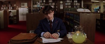 Movie still from “Rushmore” (1998), directed by Wes Anderson – A man sitting at a table in front of papers; Medium shot, Low angle