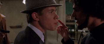 Movie still from “Rushmore” (1998), directed by Wes Anderson – A young man wearing a hat is touching his finger to his lips; Close Up shot, Over the shoulder angle