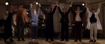 Movie still from “Rushmore” (1998), directed by Wes Anderson – A group of people holding their hands up in the air; Wide shot, Low angle