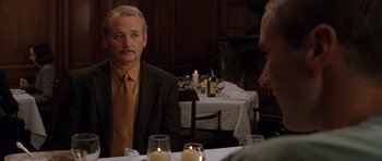 Movie still from “Rushmore” (1998), directed by Wes Anderson – A man sitting in front of a table in front of candles; Medium shot, Over the shoulder angle