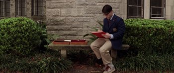 Movie still from “Rushmore” (1998), directed by Wes Anderson – A man sitting on top of a bench writing on a piece of paper; Wide shot, High angle
