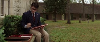 Movie still from “Rushmore” (1998), directed by Wes Anderson – A man sitting on a bench holding a book; Medium shot, Over the shoulder angle