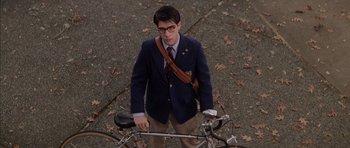Movie still from “Rushmore” (1998), directed by Wes Anderson – A man in a jacket and tie standing next to a bicycle; Wide shot, High angle