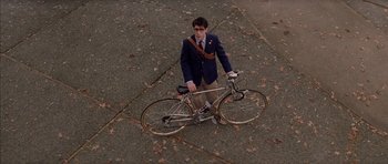 Movie still from “Rushmore” (1998), directed by Wes Anderson – A man in a suit and tie standing next to a bicycle; Wide shot, High angle
