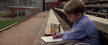 Movie still from “Rushmore” (1998), directed by Wes Anderson – A young boy is writing on a piece of paper; Medium shot, Low angle
