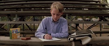 Movie still from “Rushmore” (1998), directed by Wes Anderson – A young boy sitting at a park bench writing in a notebook; Medium shot, Low angle