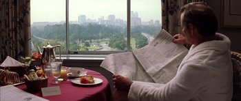 Movie still from “Rushmore” (1998), directed by Wes Anderson – A person sitting at a table reading a newspaper; Wide shot, Over the shoulder angle