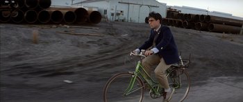 Movie still from “Rushmore” (1998), directed by Wes Anderson – A man is riding a bike in the street; Wide shot, Low angle