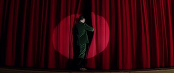 Movie still from “Rushmore” (1998), directed by Wes Anderson – A man standing in front of a red stage curtain; Wide shot, Low angle