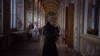 Movie still from “Russian Ark” (2002), directed by Aleksandr Sokurov – An older woman in a black coat in an ornate hallway; Medium shot, Over the shoulder angle