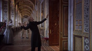 Movie still from “Russian Ark” (2002), directed by Aleksandr Sokurov – An older woman in a black coat is in an ornate hallway; Wide shot, Low angle