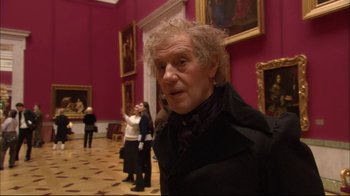 Movie still from “Russian Ark” (2002), directed by Aleksandr Sokurov – An older man standing in front of a wall of paintings; Medium shot, Over the shoulder angle
