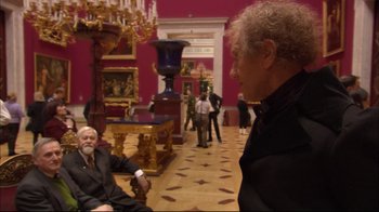Movie still from “Russian Ark” (2002), directed by Aleksandr Sokurov – Two men in suits in a room with a red wall; Wide shot, High angle