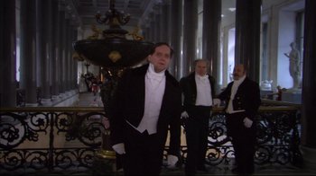 Movie still from “Russian Ark” (2002), directed by Aleksandr Sokurov – A group of men dressed in formal attire standing in front of a fountain; Wide shot, Low angle