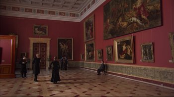 Movie still from “Russian Ark” (2002), directed by Aleksandr Sokurov – A woman in a long black dress standing in front of a wall of paintings; Extreme Wide shot, High angle