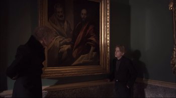 Movie still from “Russian Ark” (2002), directed by Aleksandr Sokurov – A woman standing next to a large painting of a man; Medium shot, Over the shoulder angle