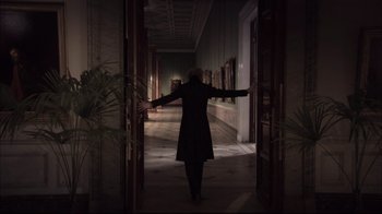 Movie still from “Russian Ark” (2002), directed by Aleksandr Sokurov – A woman standing in a dark hallway with her arms outstretched; Wide shot, Over the shoulder angle