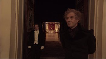 Movie still from “Russian Ark” (2002), directed by Aleksandr Sokurov – Two men dressed up in formal wear in a dark room; Medium shot, Over the shoulder angle