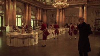 Movie still from “Russian Ark” (2002), directed by Aleksandr Sokurov – A group of men in red suits standing in front of tables with food; Wide shot, High angle