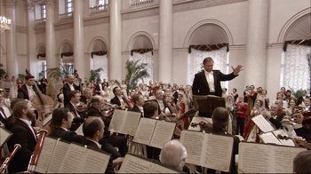 Movie still from “Russian Ark” (2002), directed by Aleksandr Sokurov – A large group of people sitting and standing in front of a conductor; Extreme Wide shot, Low angle
