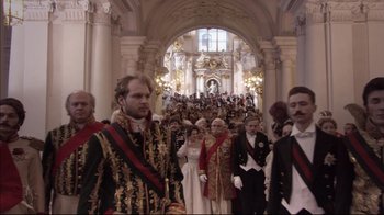 Movie still from “Russian Ark” (2002), directed by Aleksandr Sokurov – A group of people in formal wear standing in front of an archway; Wide shot, Over the shoulder angle
