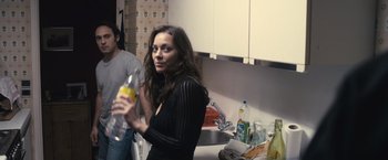 Movie still from “Rust and Bone” (2012), directed by Jacques Audiard – A woman holding a bottle in a kitchen; Medium shot, Over the shoulder angle