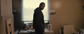 Movie still from “Rust and Bone” (2012), directed by Jacques Audiard – A man standing in front of a window in a kitchen; Medium shot, Low angle
