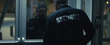 Movie still from “Rust and Bone” (2012), directed by Jacques Audiard – A security guard looking in the mirror of a building; Medium shot, Over the shoulder angle