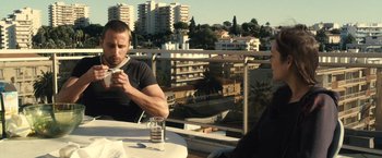Movie still from “Rust and Bone” (2012), directed by Jacques Audiard – A man sitting at a table drinking a cup of coffee; Medium shot, Low angle